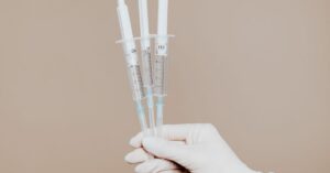 A gloved hand holding three injections of peptide therapy