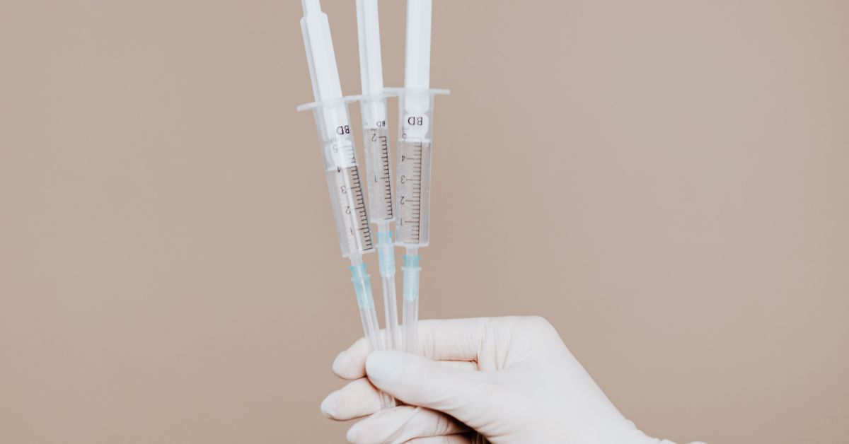 A gloved hand holding three injections of peptide therapy