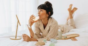 A woman drinking a glass of white wine on her bed.