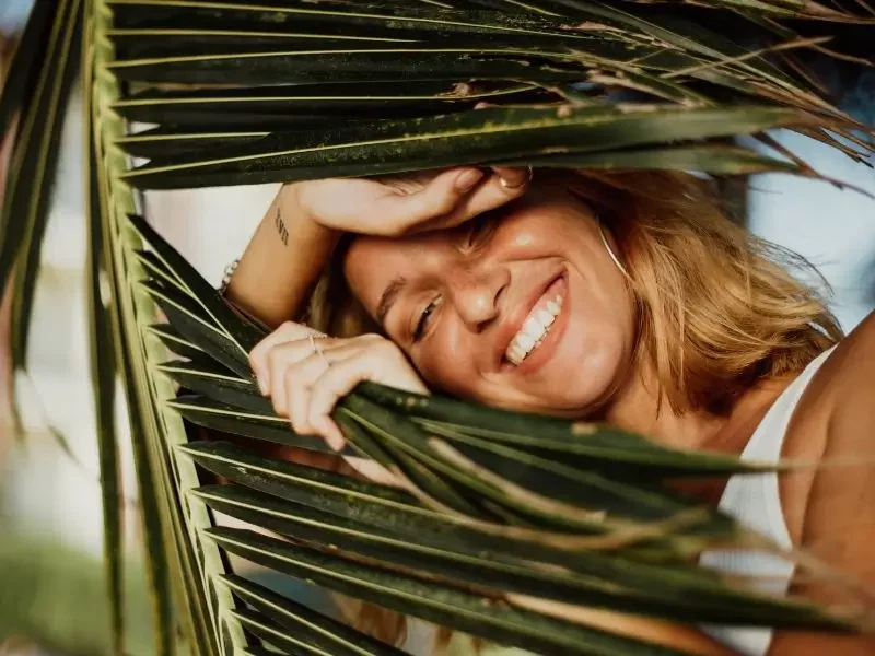 Gut-digestive-issues Happy woman, peeking out through a palm tree because she healed her digestive issues.